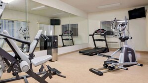 Un gimnasio con máquinas de cardio, un espejo grande y un televisor en la pared.