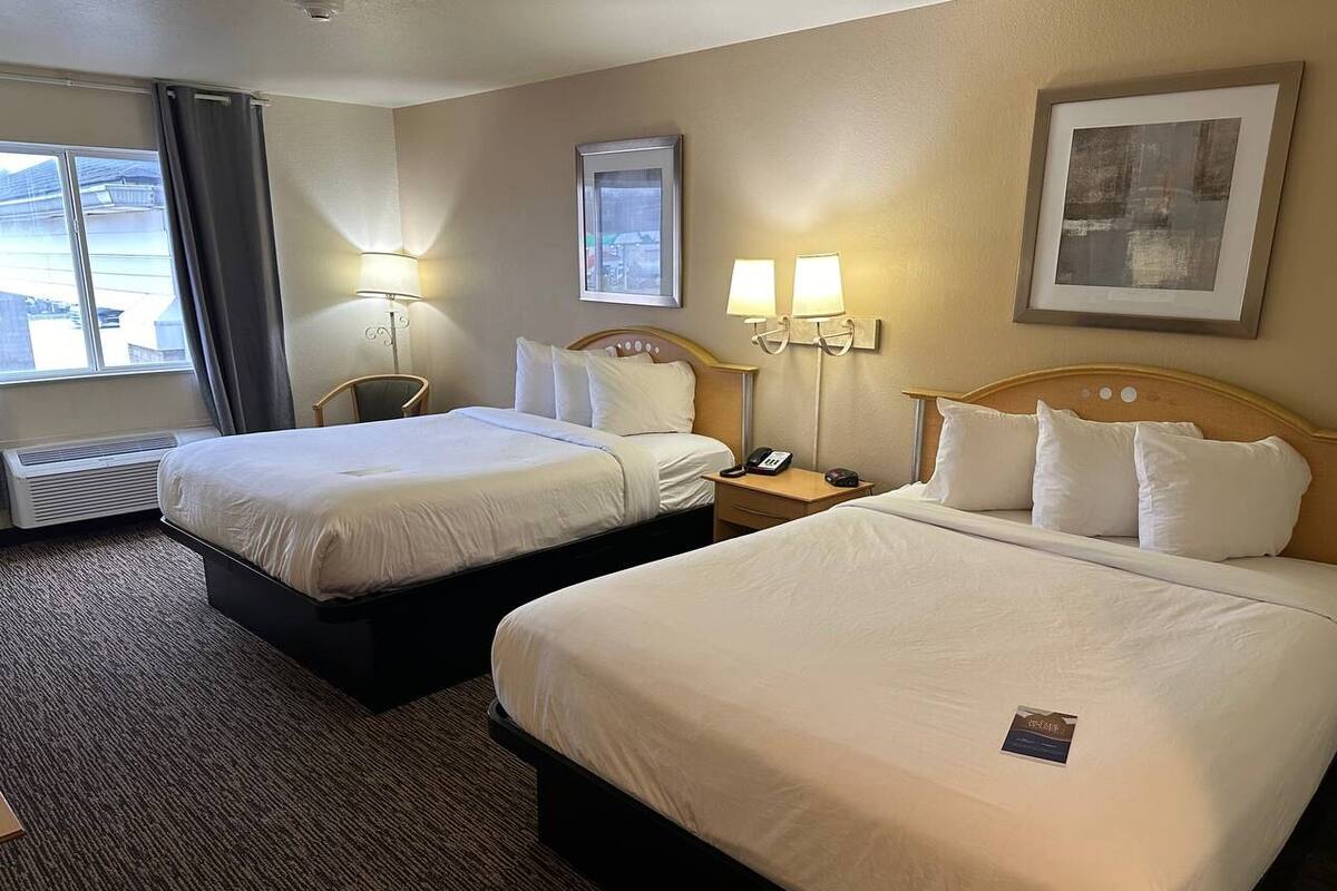 Une chambre d’hôtel avec deux lits, un bureau, une chaise, une lampe et une fenêtre avec des rideaux.