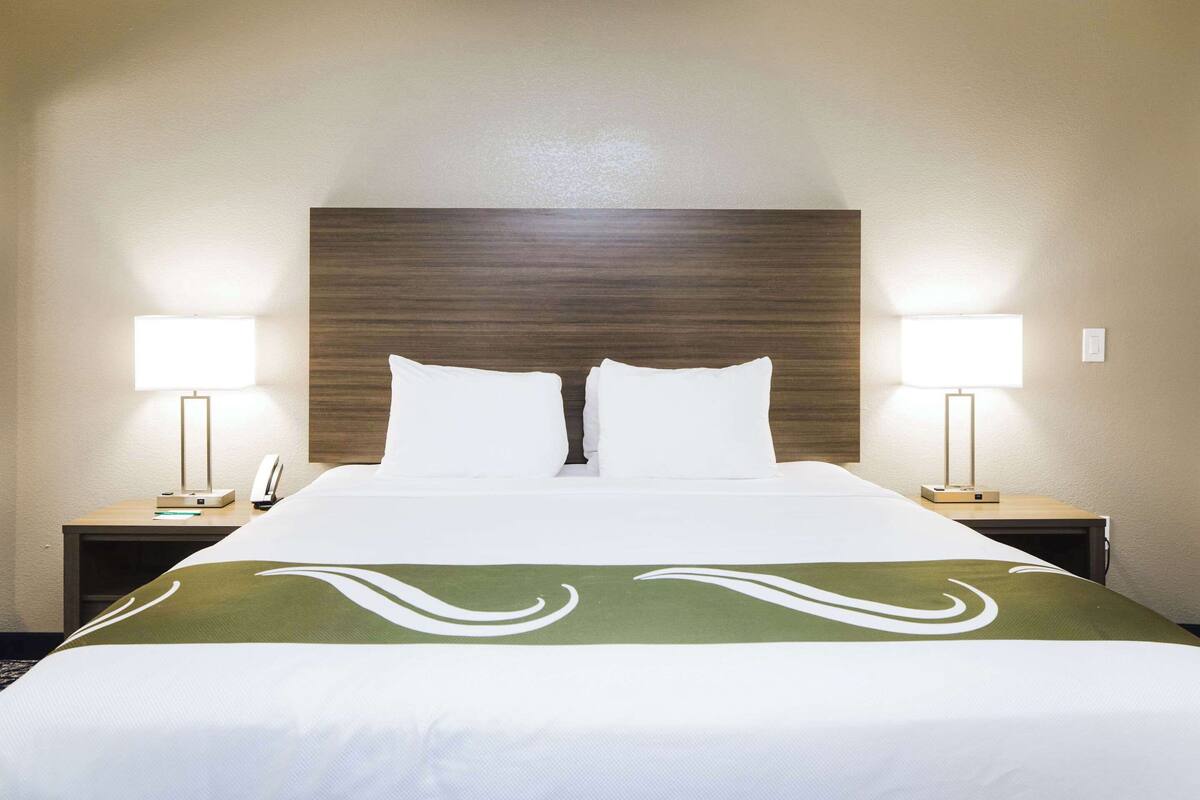 A hotel room with a large bed, two bedside tables with lamps, and a green decorative bedspread.