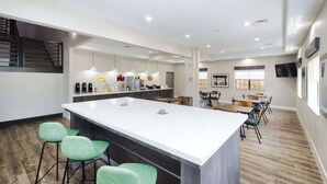 A modern kitchen with a large island, bar stools, and a dining area with tables and chairs. - Quality Suites Houston Hobby Airport (Houston)