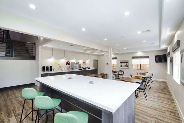 A modern kitchen with a large island, bar stools, and a dining area with tables and chairs.