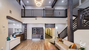 A spacious lobby with a reception desk, a seating area with a sofa and a coffee table, a staircase with a wooden railing, and a hallway leading to other areas. - Quality Suites Houston Hobby Airport (Houston)