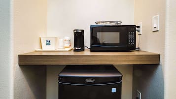 Una encimera de cocina con un microondas, una cafetera y un cubo de basura.