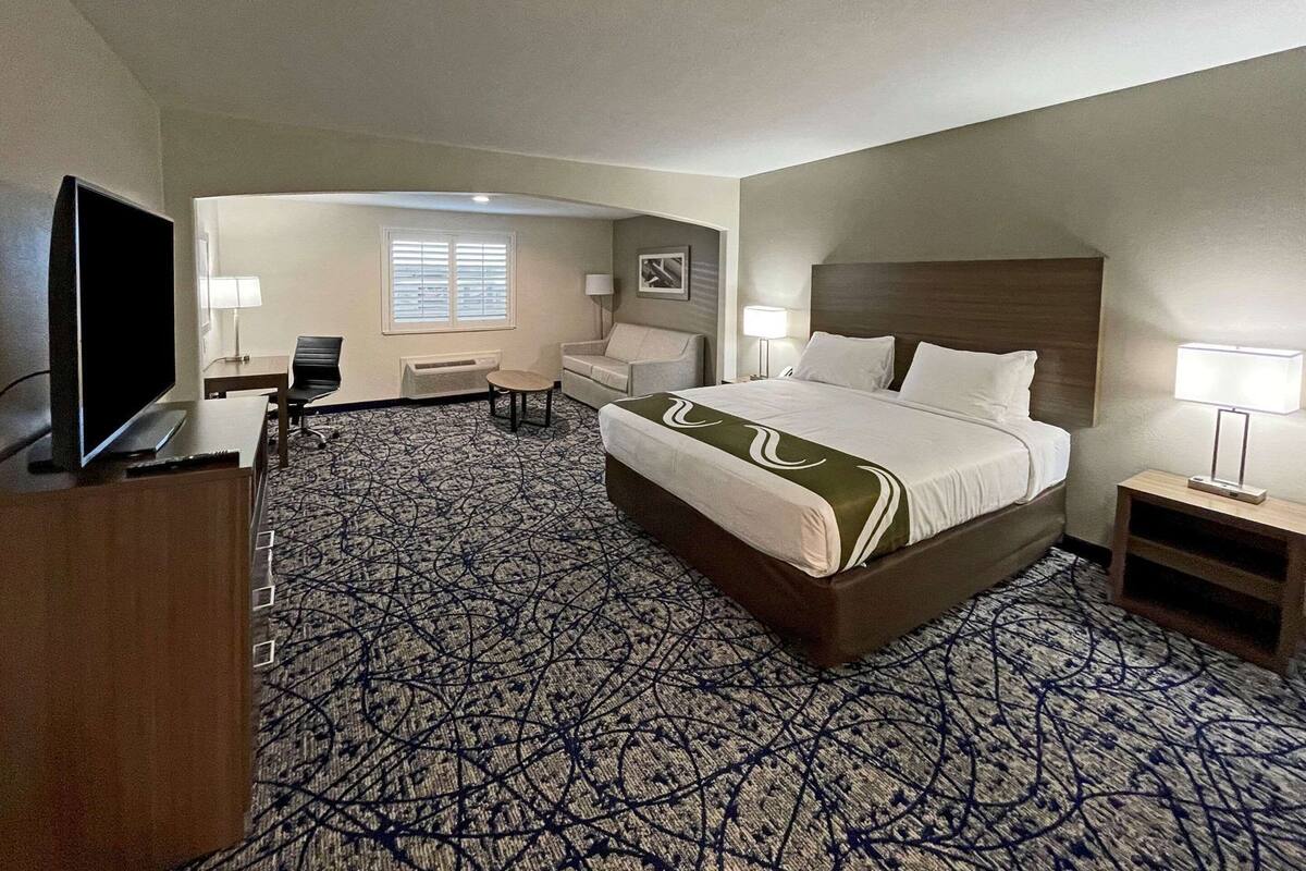 A hotel room with a large bed, a TV, a desk, and a chair.