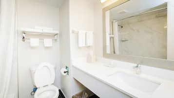 A bathroom with a toilet, sink, and shower. There are towels and a trash bin.