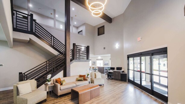 A spacious living area with a wooden staircase, a sofa set, a coffee table, and a large window providing a view of the outside. - Quality Suites Houston Hobby Airport (Houston)