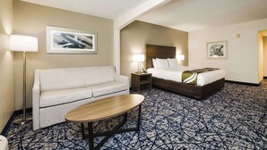 A hotel room with a sofa, a bed, a nightstand, a lamp, and a patterned carpet. - Quality Suites Houston Hobby Airport (Houston)