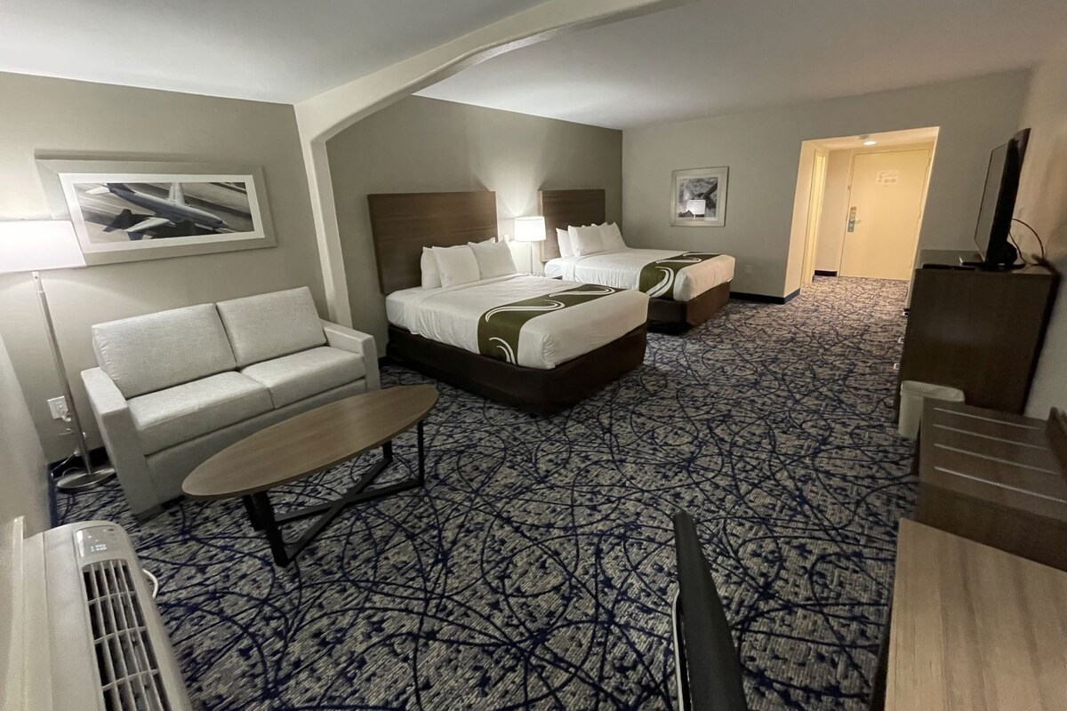 A hotel room with a sofa, two beds, a TV, and a patterned carpet.