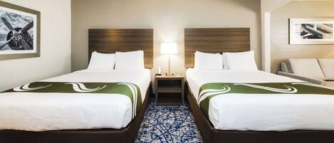 A hotel room with two beds, a nightstand, a lamp, and a framed picture on the wall.