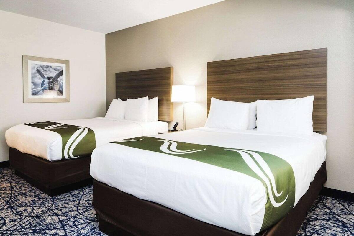 A hotel room with two beds, a headboard, a lamp, and a framed picture on the wall.