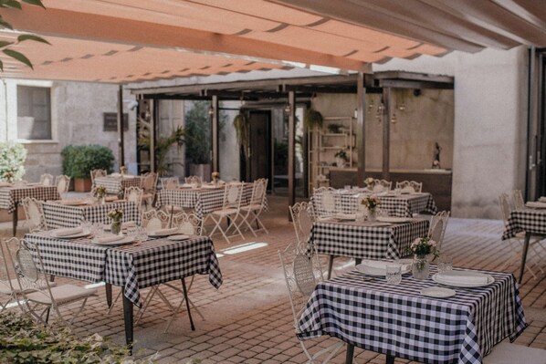 Un espace extérieur aménagé pour les repas, avec des nappes à carreaux, des chaises blanches et un patio couvert.