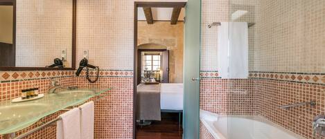 A bathroom with a glass shower enclosure, a glass sink, and a bed visible through an open doorway.