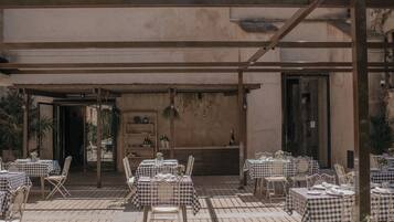 An outdoor patio with checkered tablecloths and metal chairs, surrounded by a building with a rustic appearance.