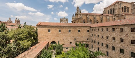 Un patio con una fuente central, rodeado de edificios de piedra con paseos arqueados y un edificio grande y ornamentado al fondo.