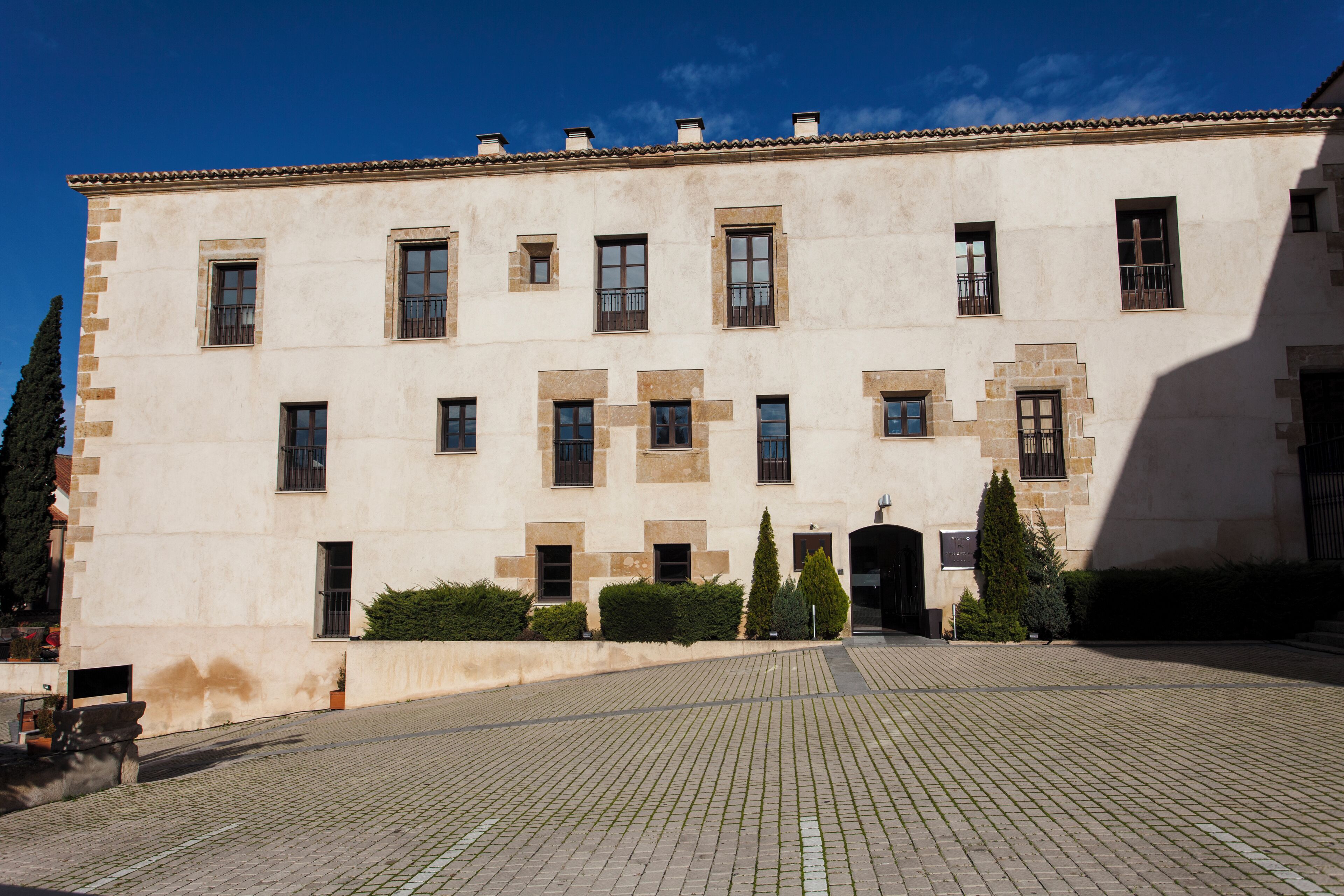 Un edificio histórico con fachada simétrica, múltiples ventanas y un patio empedrado.