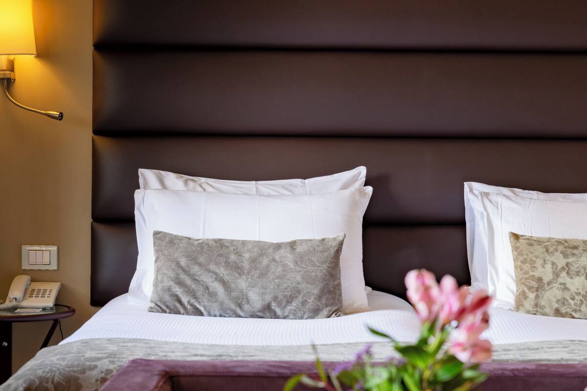 Een hotelkamer met een bed, nachtkastje, telefoon en een vaas met bloemen.