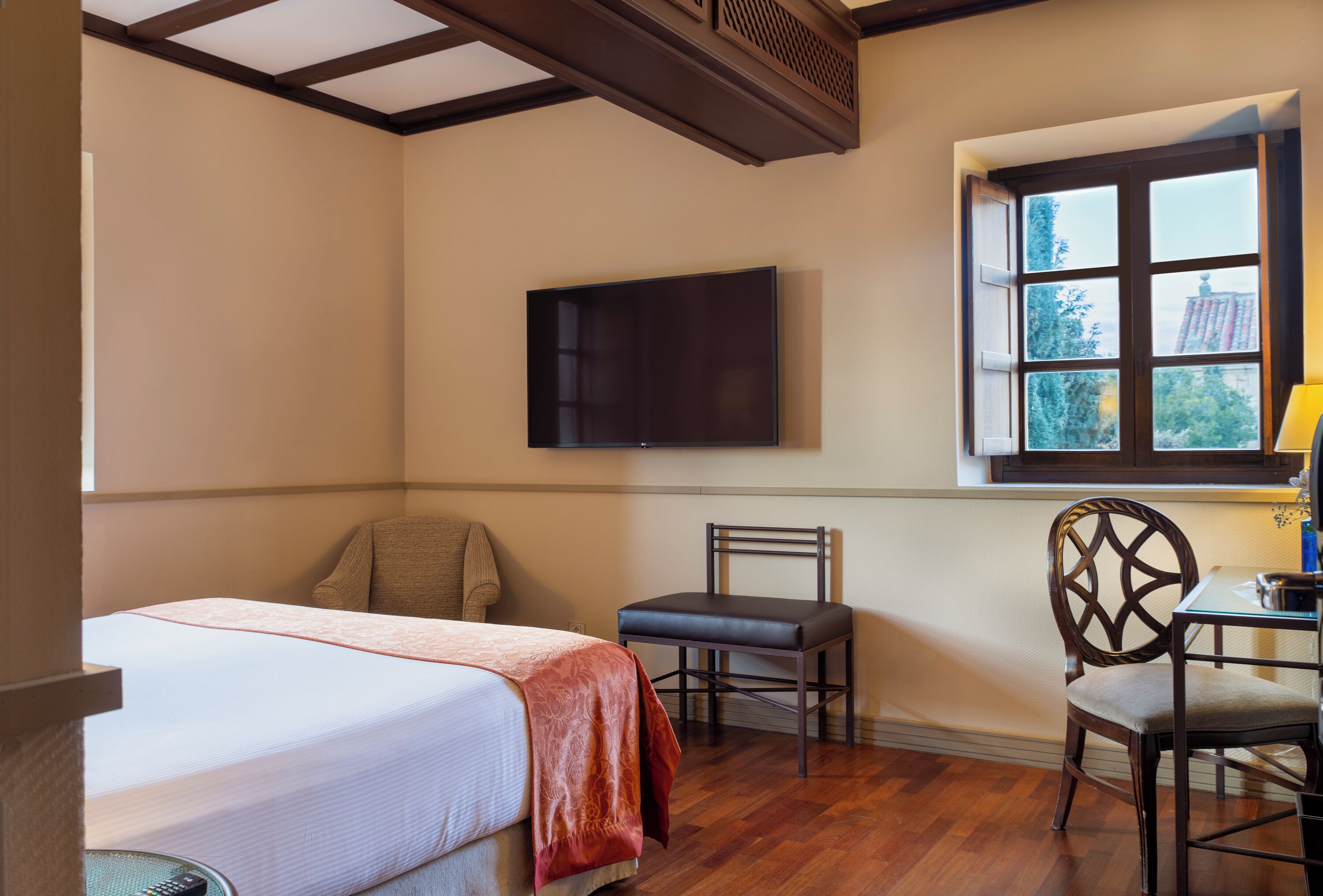 A hotel room with a bed, two chairs, a desk, a TV, and a window with a view.