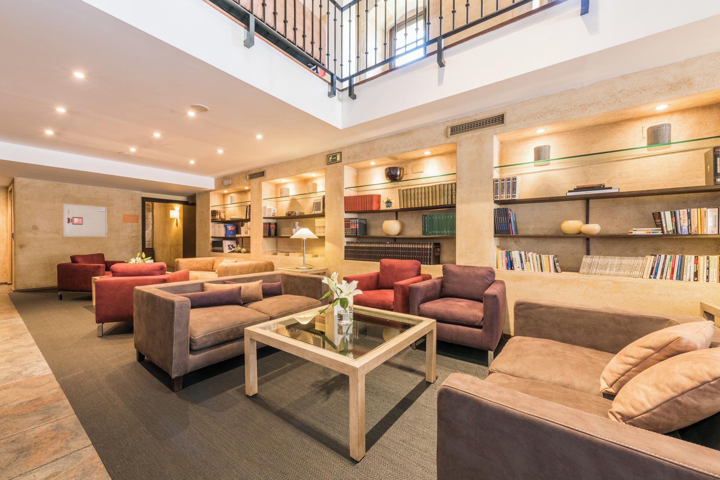 A spacious lobby with multiple seating areas, a glass coffee table, and a bookshelf filled with books.