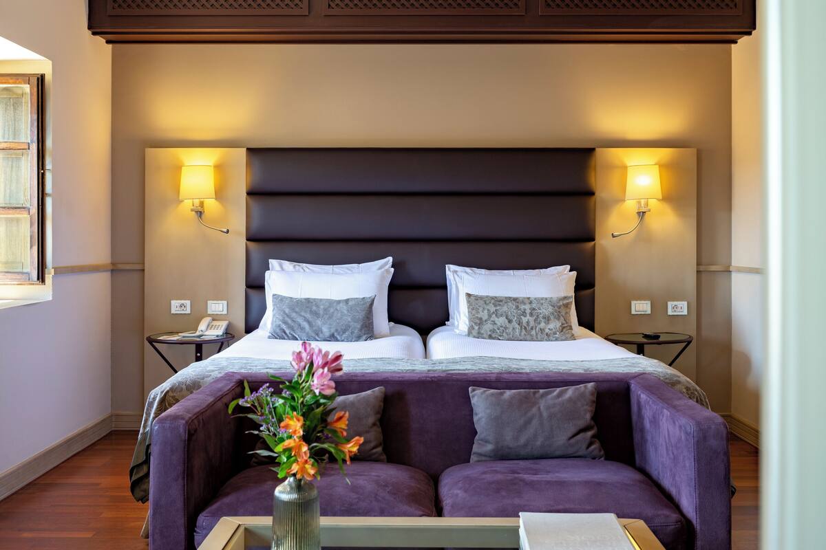 Een hotelkamer met een groot bed, twee nachtkastjes, een slaapbank en een bloemenvaas.