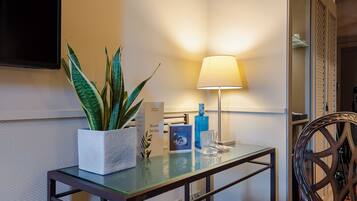 Una habitación de hotel con una mesa de vidrio, una planta en maceta, una lámpara y una silla.