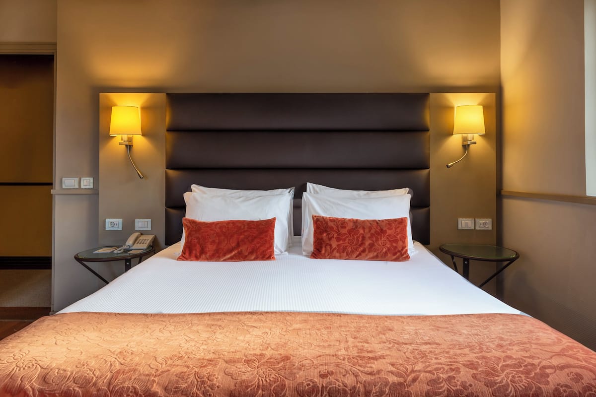 Hotelkamer met een groot bed, twee rode kussens, een donker hoofdeinde en twee wandlampen.