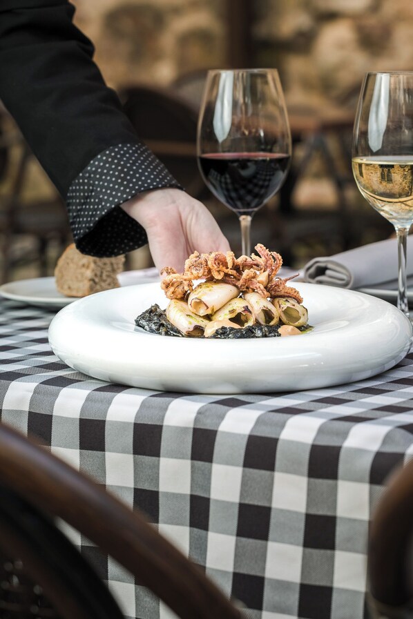A plate of pasta with seafood and a glass of red wine on a table with a checkered tablecloth.