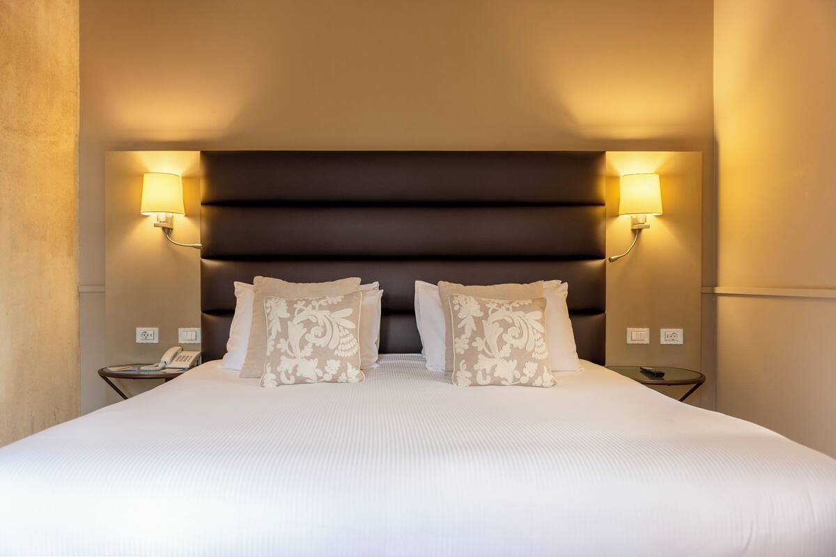 Een hotelkamer met een groot bed, twee bedlampjes, een telefoon en een klein tafeltje.