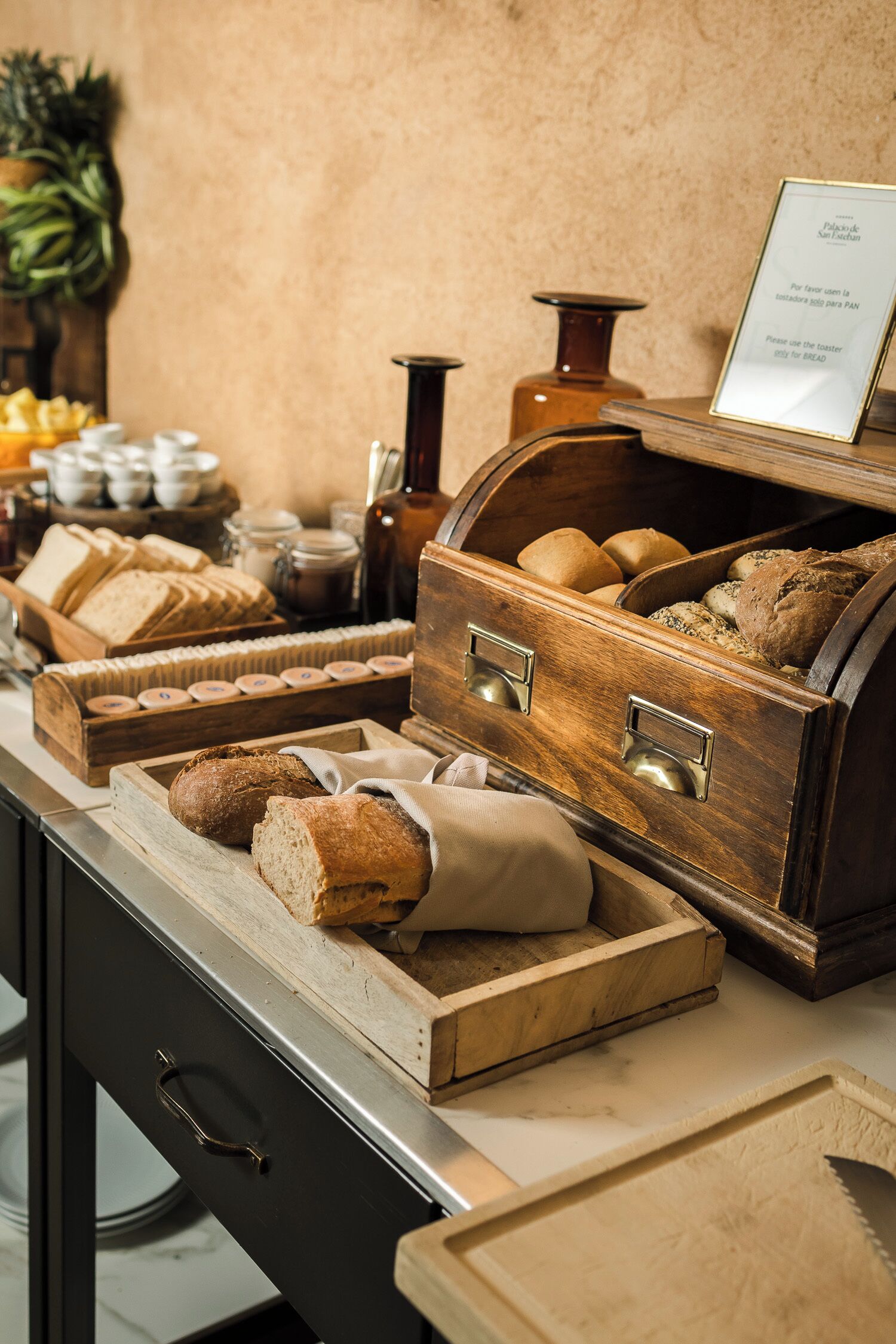 Exhibición de panadería con diversos panes y pasteles, cestas de madera para pan y un letrero con información de la panadería.