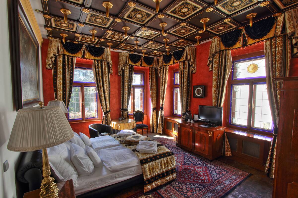 A room with a large bed, a desk with a television, and a patterned rug.