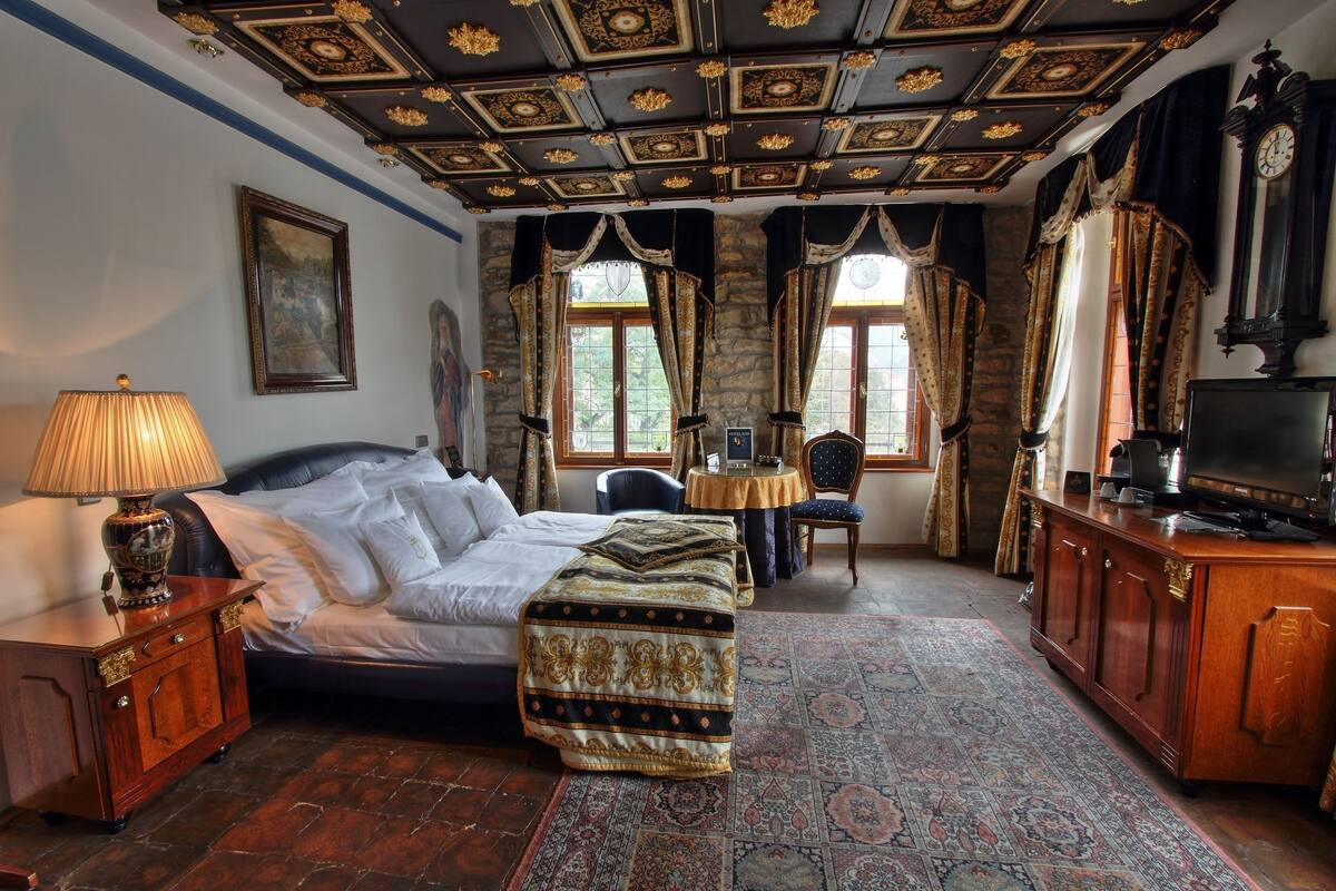 A bedroom with a large bed, a desk, a television, and a clock.