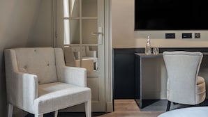 Une pièce dotée d’un grand téléviseur à écran plat fixé au mur, d’un coin salon avec deux fauteuils, d’une petite table avec des verres et d’une porte avec un miroir.