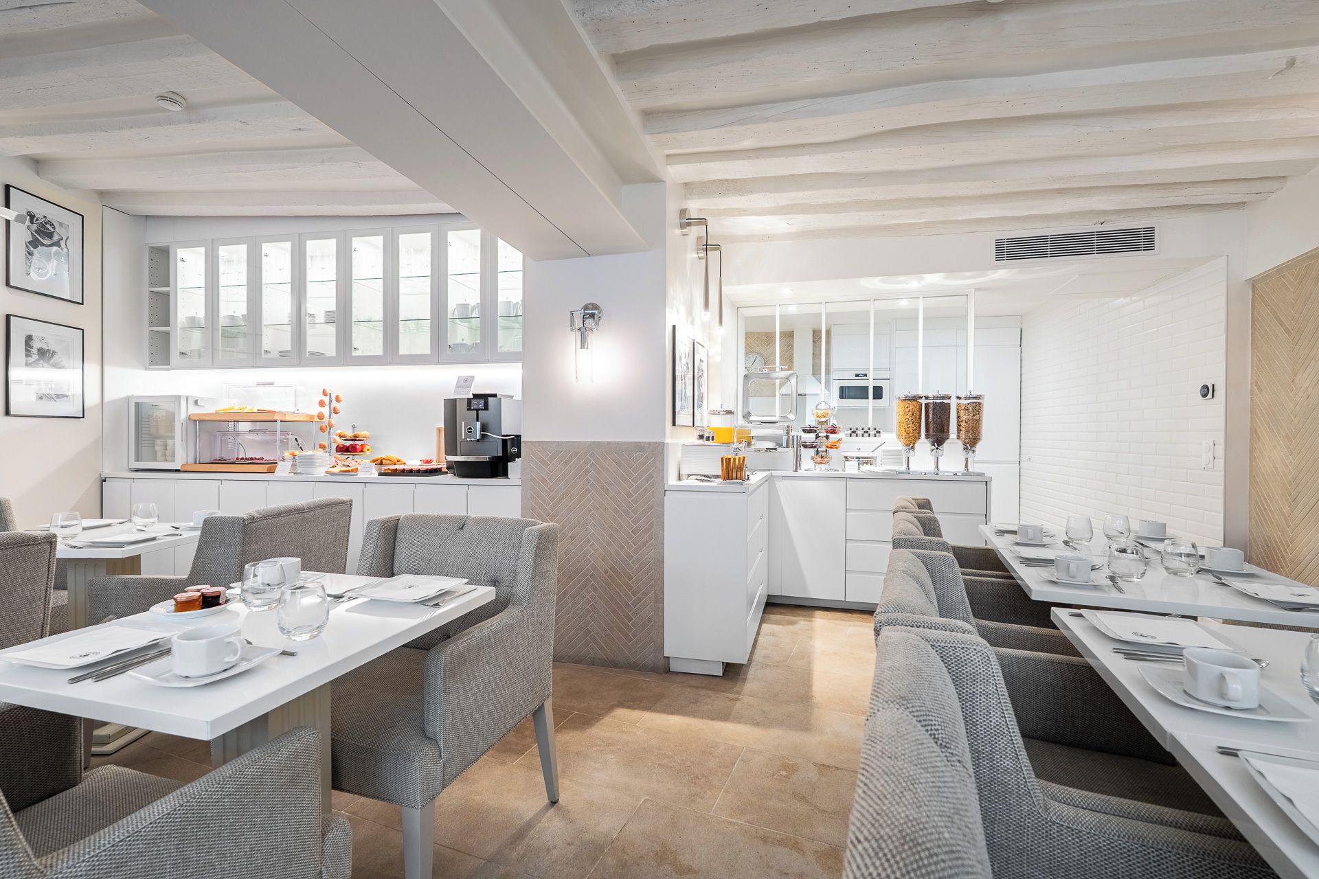 A modern dining area with white furniture, a kitchen in the background, and a herringbone-patterned wall.