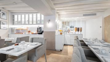 Un comedor moderno con mobiliario blanco, una cocina al fondo y una pared con motivo de espiga.
