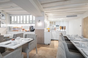 A modern dining area with white furniture, a kitchen in the background, and a herringbone-patterned wall. - Hôtel Villa d'Estrées - Saint-Germain (Paris)
