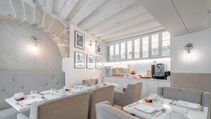 A modern dining area with high ceilings, exposed brick walls, and a kitchen area with a coffee machine. - Hôtel Villa d'Estrées - Saint-Germain (Paris)
