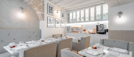 A modern dining area with high ceilings, exposed brick walls, and a kitchen area with a coffee machine.