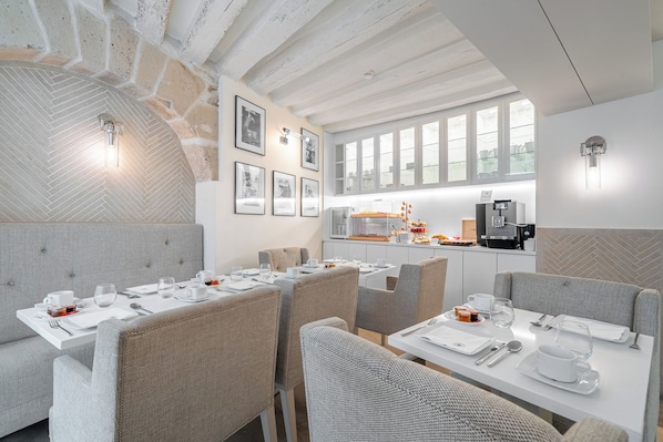 A modern dining area with high ceilings, exposed brick walls, and a kitchen area with a coffee machine.