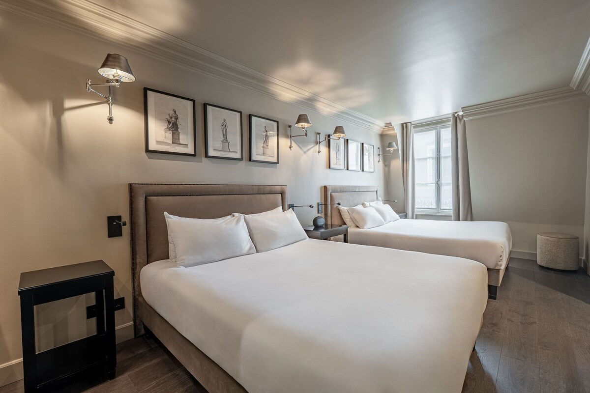 A hotel room with two beds, a nightstand, a lamp, and framed artwork on the wall.