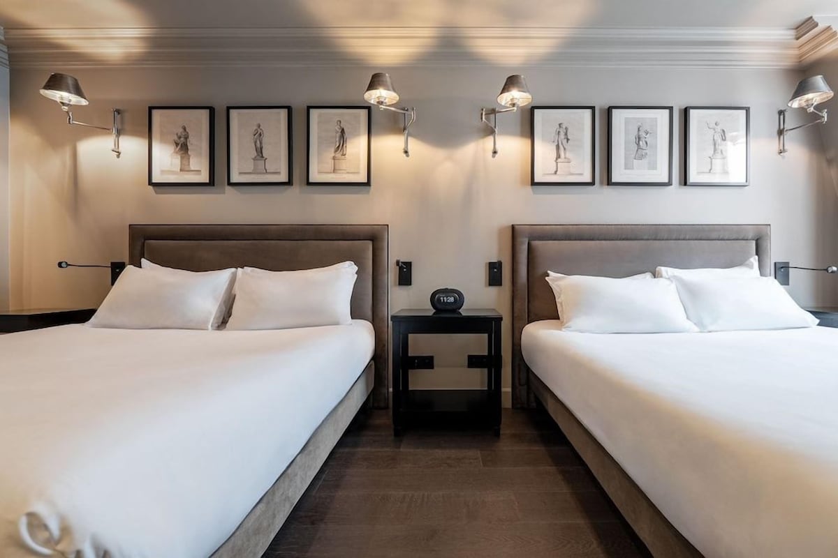 Een hotelkamer met twee bedden, een nachtkastje met een klok en wandlampen.