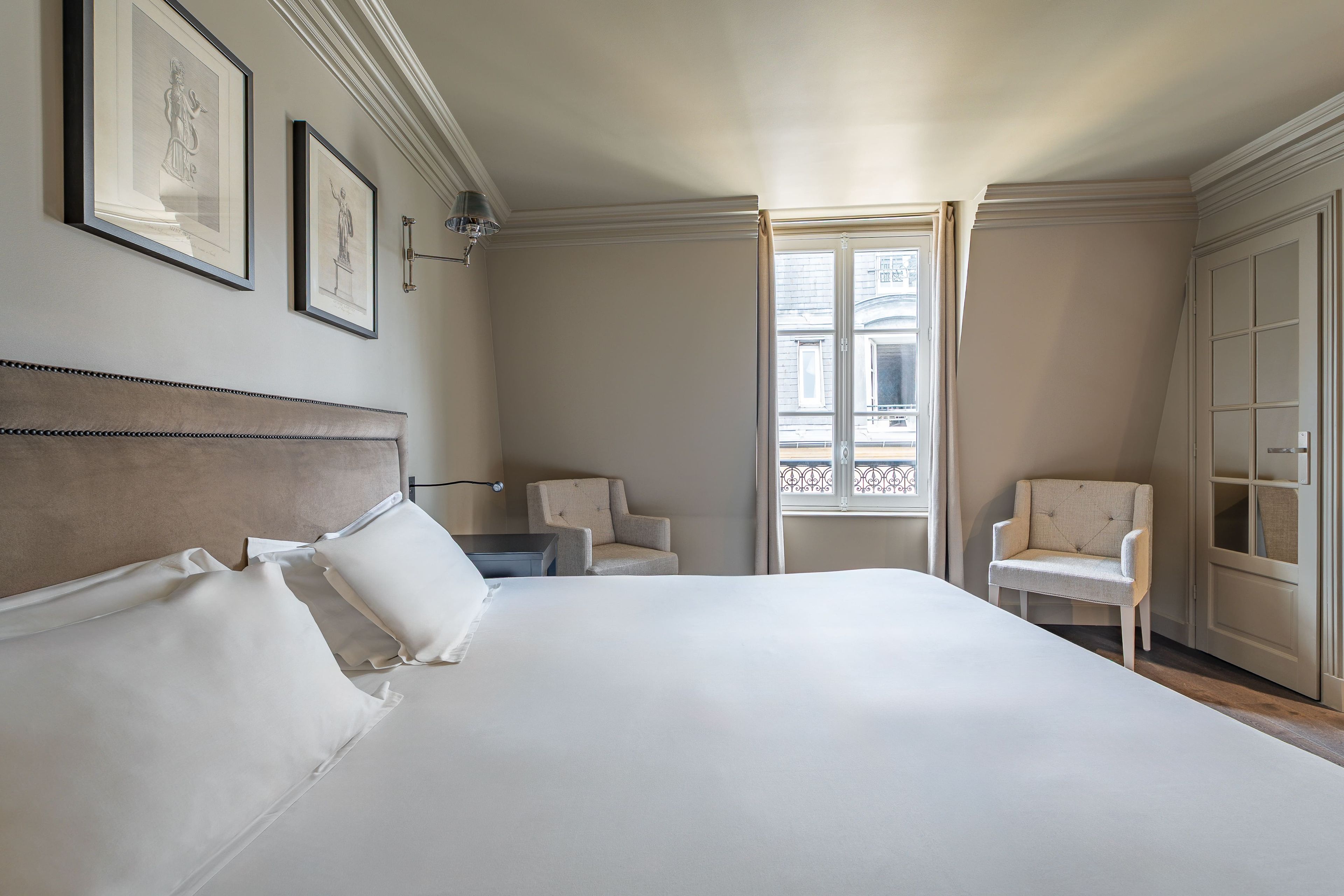 Habitación de hotel con una cama grande, dos sillones, una mesita de noche y una ventana con vista a la calle.