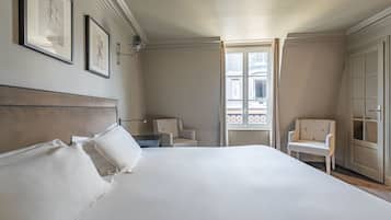 Habitación de hotel con una cama grande, dos sillones, una mesita de noche y una ventana con vista a la calle.