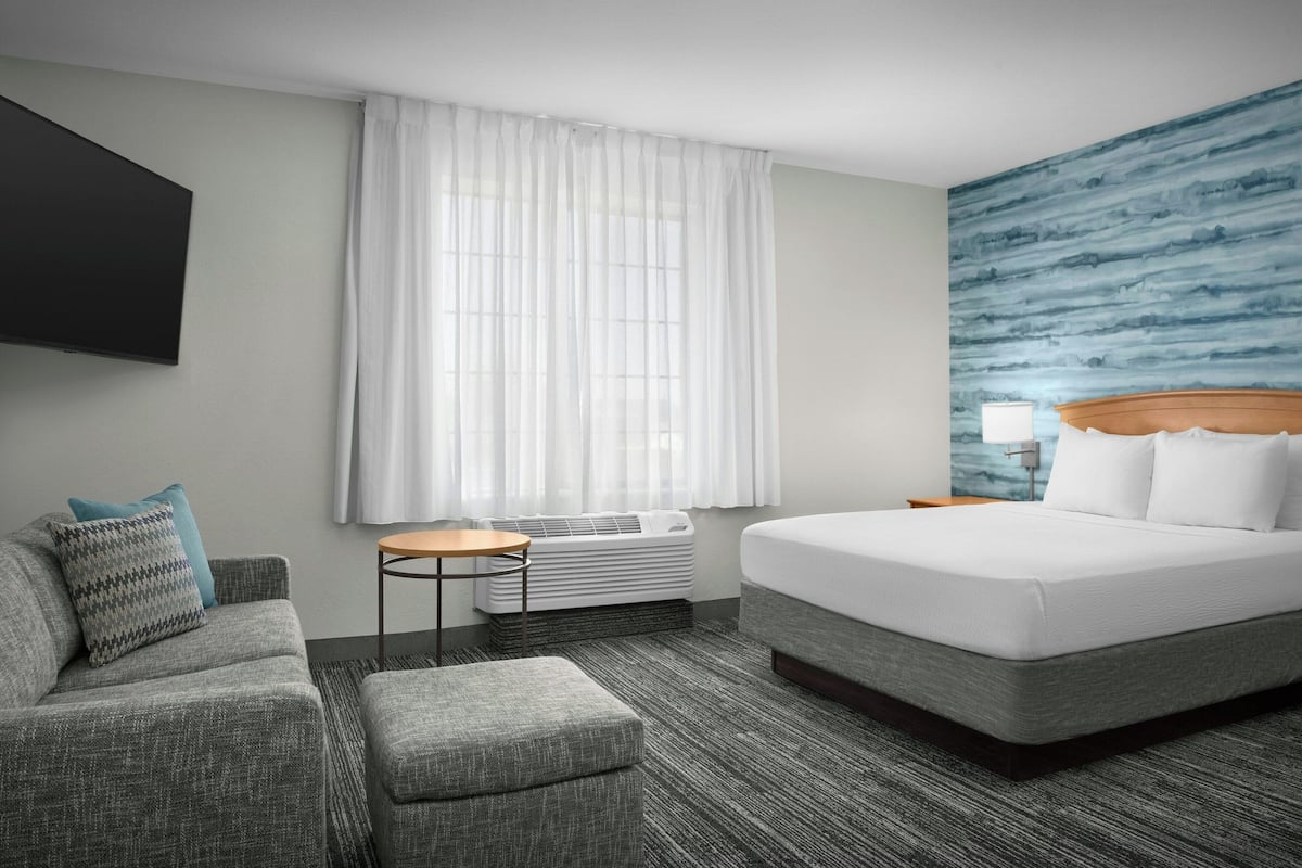 Ein Hotelzimmer mit einem großen Bett, einer Couch, einem kleinen Tisch und einem am Wand befestigten Fernseher.