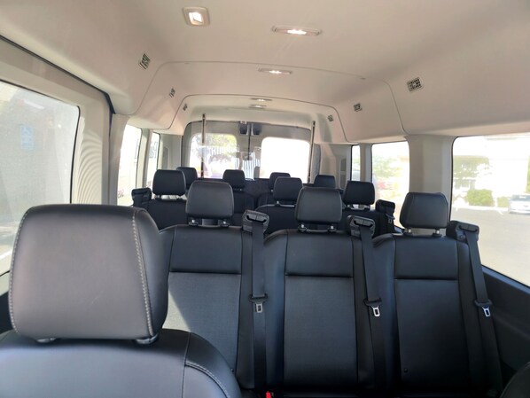A vehicle interior with multiple rows of black seats, a central aisle, and overhead storage compartments.
