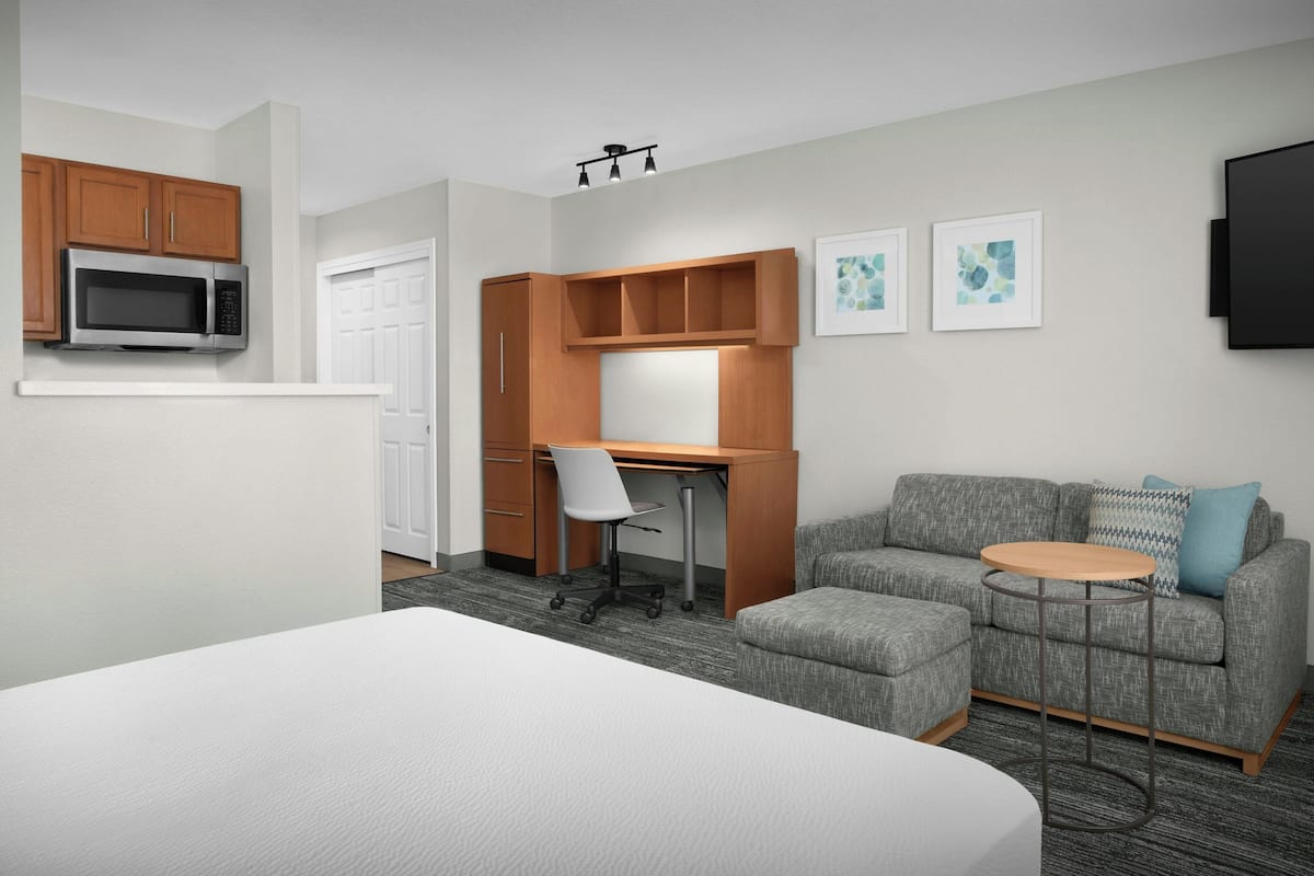 Ein Hotelzimmer mit einem Bett, einem Schreibtisch mit Stuhl, einem grauen Sofa, einem kleinen runden Tisch und einem an der Wand befestigten Fernseher.