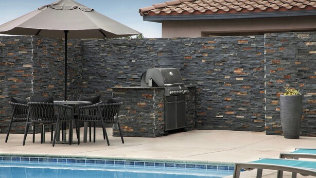 An outdoor pool area with a stone wall, a grill, and a table with chairs. - Towneplace Suites Abq Airport (Albuquerque)