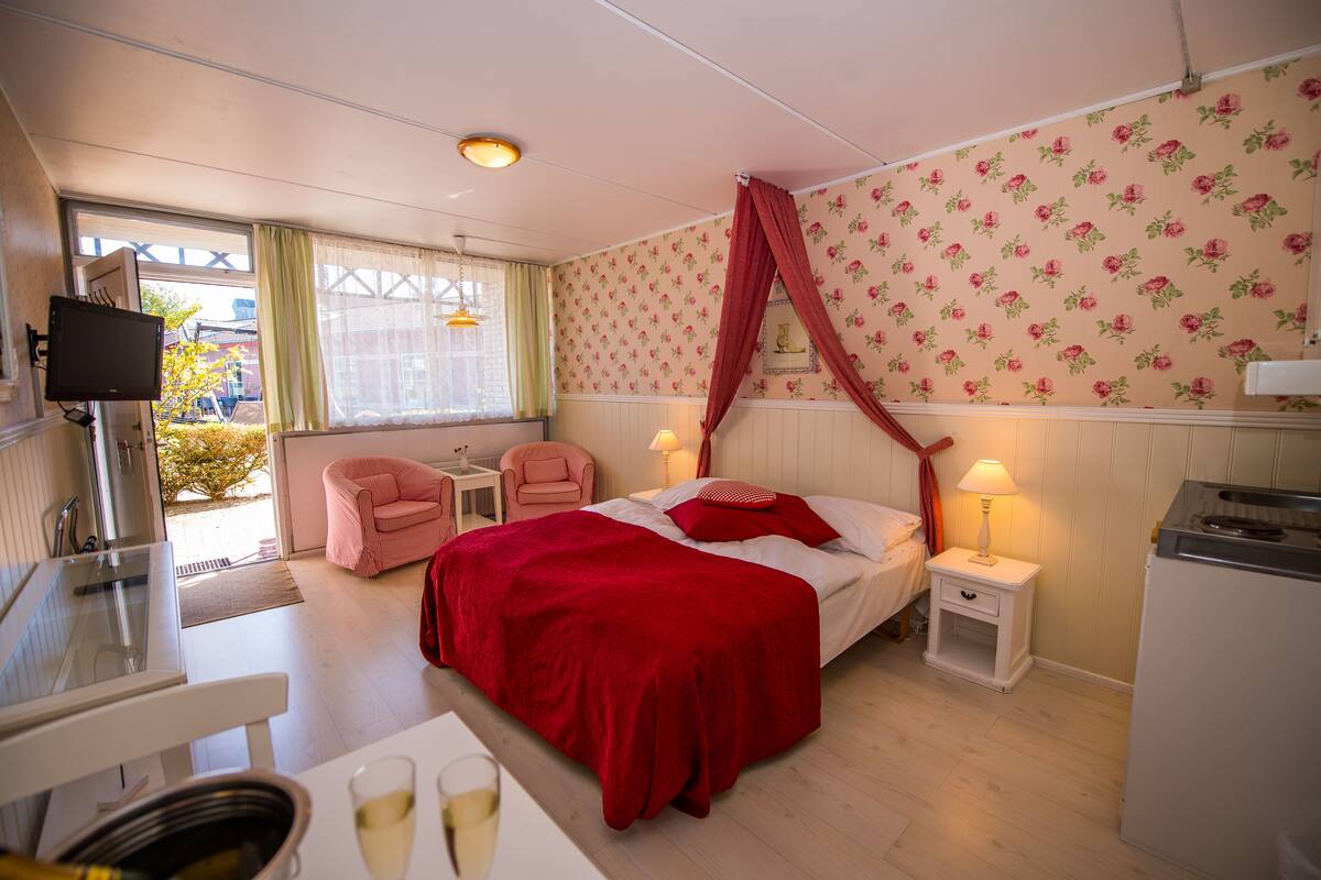 A bedroom with a bed, a desk, a chair, a TV, and a window.