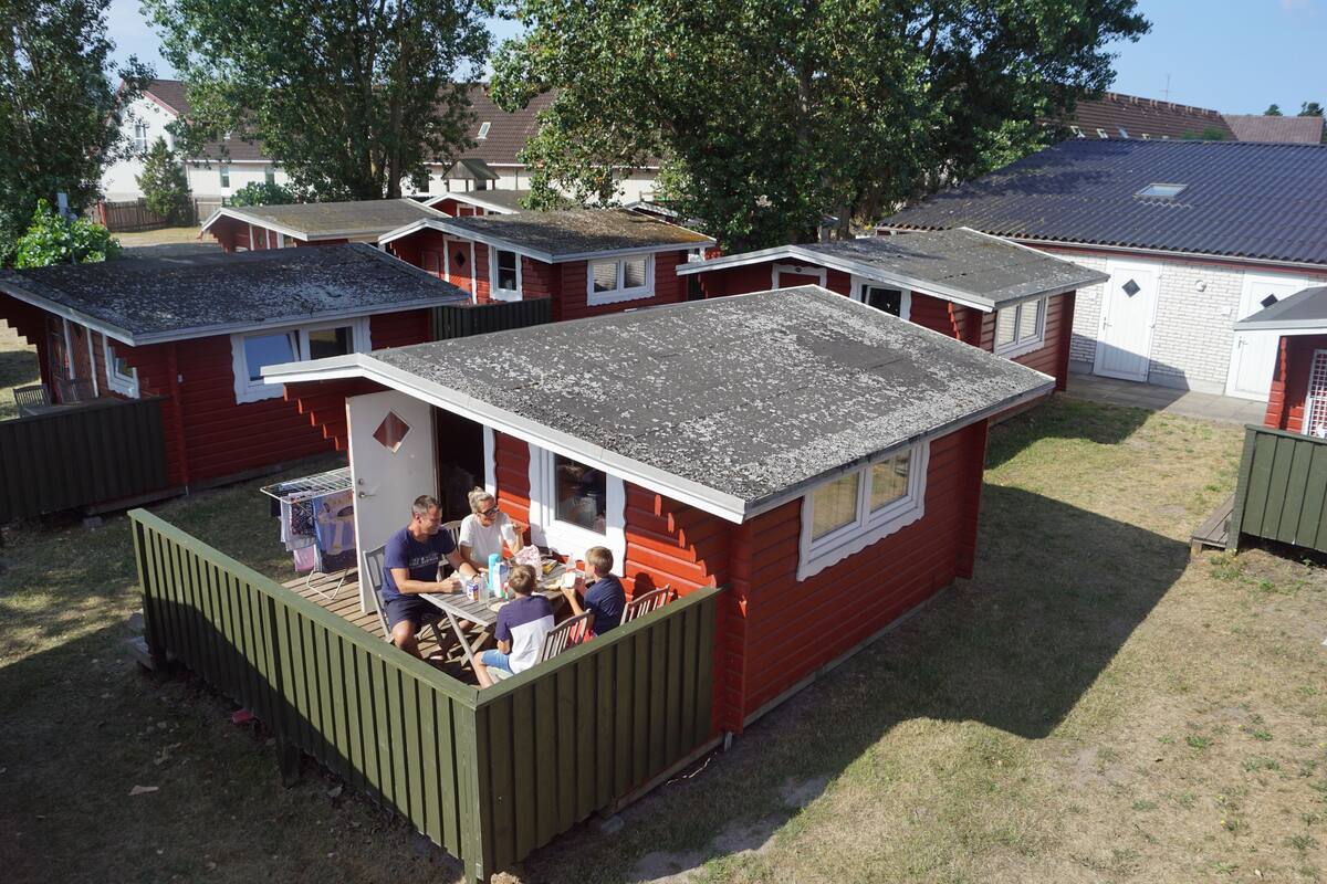 A small, red mobile home with a porch area where a group of people are seated at a table.