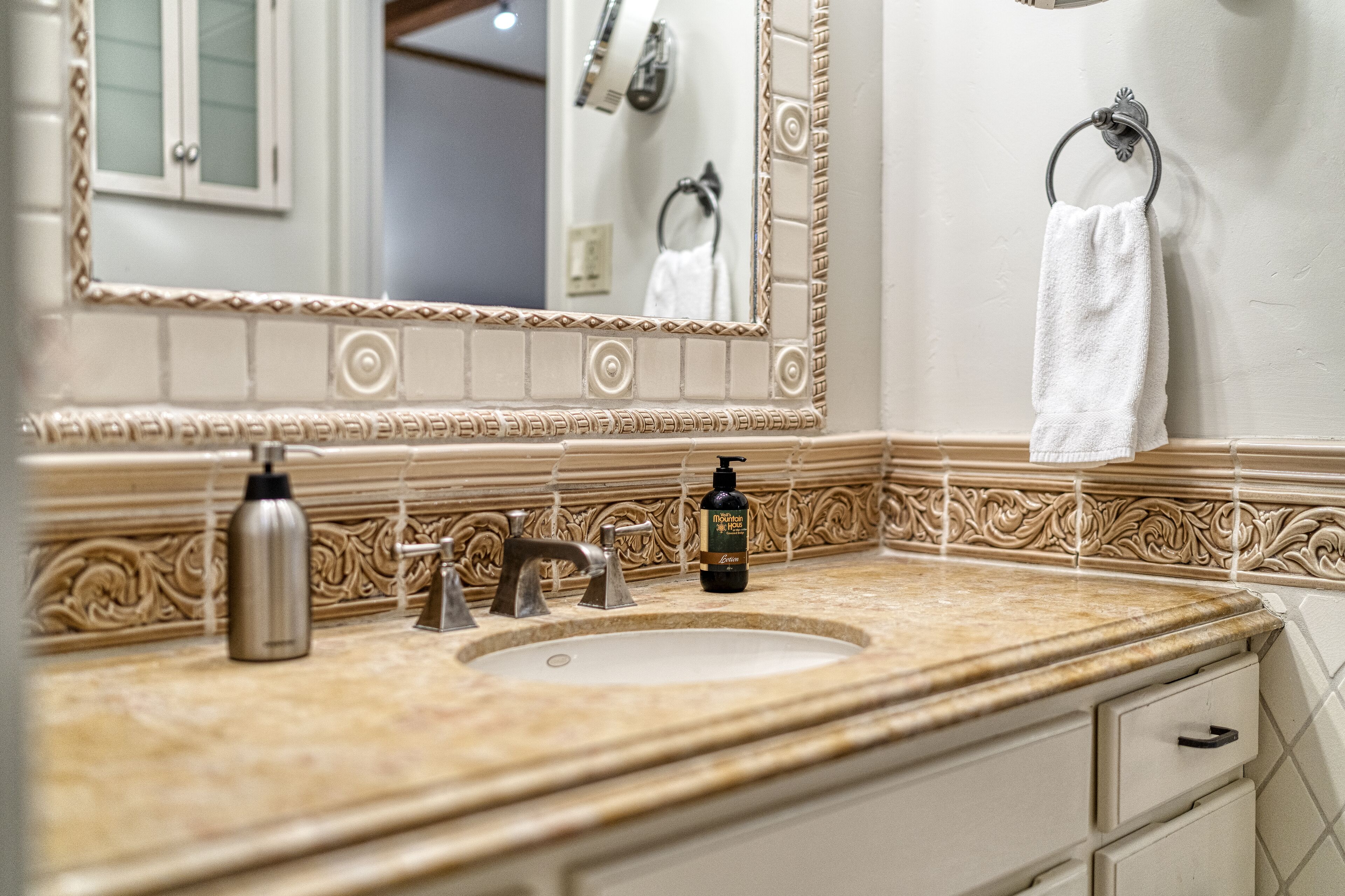 A bathroom with a sink, a mirror, a towel rack, and a bottle of shampoo.