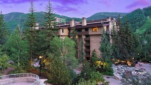Un hotel de varios pisos con un diseño moderno, rodeado de exuberante vegetación y montañas.