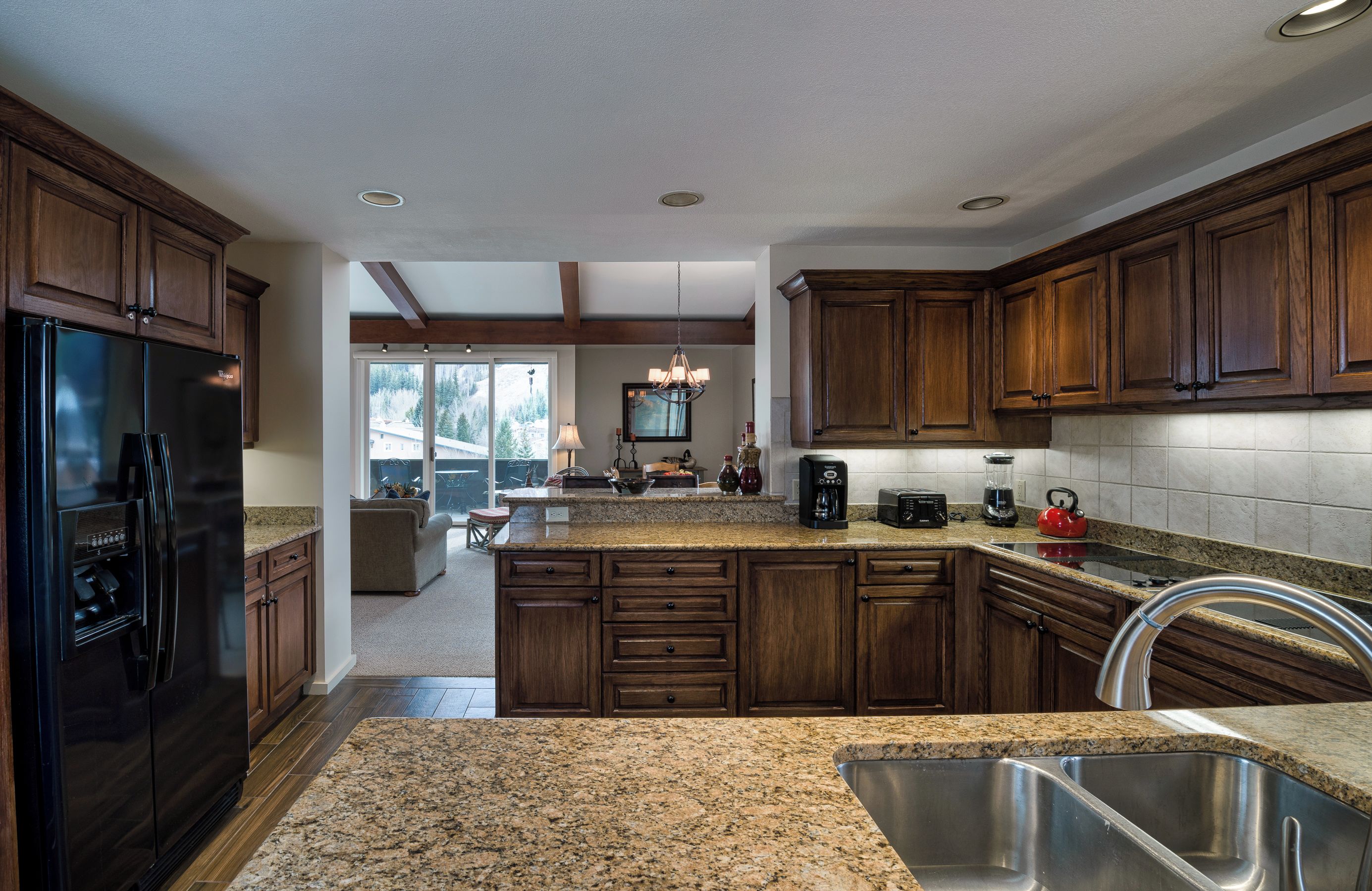 A kitchen with dark wooden cabinets, granite countertops, a stainless steel sink, and a built-in oven.